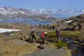 Wandergruppe auf einem Pfad in Grönland, mit Blick auf einen eisbedeckten Fjord im Hintergrund.