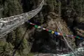 Hängebrücke mit Gebetsfahnen über einer Schlucht.