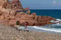 Zwei Wanderer auf einem Küstenpfad mit roten Felsen und Meerblick.