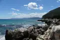 Felsige Küste mit türkisfarbenem Meer und Bergen im Hintergrund.