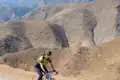 Radfahrer auf Bergstraße mit hügeliger Landschaft im Hintergrund.