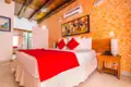 Schlafzimmer mit roter Tagesdecke, orangen Wänden, Klimaanlage und Nachttisch.