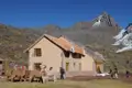 Andenhütte mit Lamas und Wanderern, schneebedeckter Gipfel im Hintergrund.