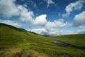 Grüne Hügellandschaft mit einem Fluss unter einem bewölkten Himmel.