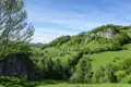 Blick auf eine grüne Hügellandschaft mit vereinzelten Häusern und bewaldeten Hängen.