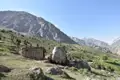 Einfache Berghütte mit Steinmauer und Holzdach vor einer Bergkulisse.
