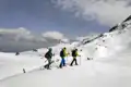 Drei Personen auf Schneeschuhen wandern durch den Schnee in den Bergen.