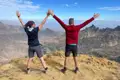 Zwei Wanderer feiern das Erreichen des Gipfels mit erhobenen Armen.