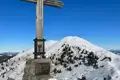 Gipfelkreuz mit Blick auf einen verschneiten Berg.