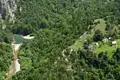 Luftaufnahme eines Flusses und einer ländlichen Siedlung, umgeben von üppiger Vegetation und bewaldeten Hügeln.