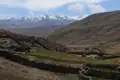 Traditionelle Behausungen und Steinmauern in einem Andental, mit Blick auf die schneebedeckten Berge.