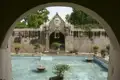 Ein Wassergarten mit Springbrunnen und einem kunstvollen Tor, gesehen durch einen Torbogen.