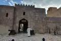 Jabreen Castle Eingang mit Kanonen und einer Person in traditioneller Kleidung.