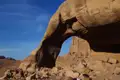 Ein natürlicher Felsbogen in der Wüste rahmt den Blick auf eine historische Stätte ein.