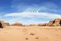 Weitläufige Wüstenlandschaft mit roten Felsformationen und einer einzigartigen Wolkenformation am blauen Himmel.