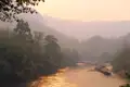 Schwimmende Unterkünfte auf einem Fluss bei Sonnenuntergang, umgeben von üppiger Vegetation und sanften Hügeln.