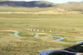 Traditionelles Jurtencamp in einer mongolischen Landschaft mit Fluss und Bergen im Hintergrund.