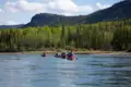 Kanufahrer auf einem Fluss mit bewaldeten Hügeln im Hintergrund.
