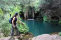 Wanderer am Ufer eines türkisfarbenen Teichs mit Wasserfall.