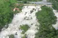 Luftansicht der Stromschnellen eines Flusses mit einer Brücke im Hintergrund.