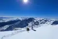 Skiausrüstung auf einem sonnigen Berggipfel mit Panoramablick auf die verschneite Bergkette.