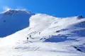 Drei Personen auf Skitour in den Bergen. Der Schnee bedeckt den gesamten Hang, und der Gipfel ist im Hintergrund zu sehen.