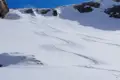 Abfahrtsspuren im frischen Schnee, umgeben von einer verschneiten Berglandschaft unter blauem Himmel.