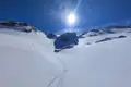 Verschneite Berglandschaft mit Spuren im Schnee und Sonnenschein.