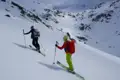 Zwei Skitourengeher fahren einen verschneiten Berg hinab.