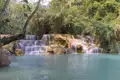 Wasserfall mit mehreren Kaskaden und türkisfarbenem Becken inmitten tropischer Vegetation.