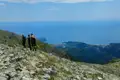 Wanderer auf einem Bergpfad mit Blick auf das Meer und eine Küstenstadt.