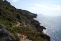 Felsige Küstenlinie mit spärlicher Vegetation und Blick auf das glitzernde Meer.