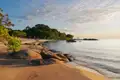 Ruhiger Strand mit goldenen Sand, Felsen und bewaldeter Küste.