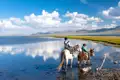 Zwei Kinder reiten auf einem Pferd und einem Esel durch einen See, umgeben von Bergen.