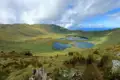 Vulkanischer Kratersee mit grüner Vegetation und umgebendem Kraterrand.