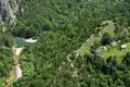 Luftaufnahme eines Flusses, der sich durch bewaldete Hügel schlängelt, mit Häusern und landwirtschaftlichen Flächen am Flussufer.