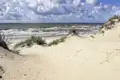 Dünen und Meer unter bewölktem Himmel.