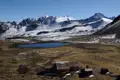 Eine Berghütte bietet Unterkunft inmitten der Andenlandschaft mit einem See und schneebedeckten Gipfeln im Hintergrund.