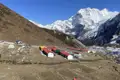 Basislager mit Unterkünften und Zelten inmitten einer Berglandschaft mit Blick auf einen schneebedeckten Gipfel.