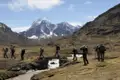 Wanderer überqueren einen Gebirgsbach in den Anden. Der schneebedeckte Gipfel im Hintergrund deutet auf die Höhe der Wanderung hin.