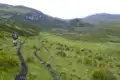 Wanderer auf einem Pfad in einer grünen Hügellandschaft.
