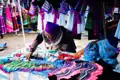 Marktverkäuferin in traditioneller Kleidung bietet handgefertigte Textilien und Waren an.