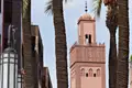 Minarett einer Moschee, teilweise verdeckt durch Palmenstämme.