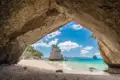 Blick durch eine Meereshöhle auf einen Sandstrand mit einzigartigen Felsformationen im türkisfarbenen Wasser.