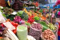Marktstand mit verschiedenen Obst- und Gemüsesorten wie Tomaten, Zwiebeln, Kartoffeln, Erbsen und Paprika.