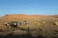 Campingplatz in der Wüste mit Zelten und Fahrzeugen, vor dem Hintergrund roter Felsformationen.