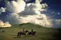 Zwei Reiter durchqueren eine weitläufige Landschaft mit sanften Hügeln unter einem beeindruckenden Himmel.