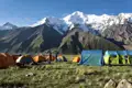 Campingplatz in den Bergen mit Zelten und schneebedeckten Gipfeln im Hintergrund.