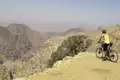Mountainbiker mit Helm und Fahrrad am Rande einer Klippe mit Blick auf eine Wüstenschlucht.