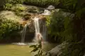 Frau unter einem Wasserfall im Dschungel.
